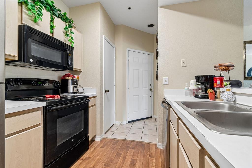 A kitchen features light wood cabinets, black appliances, a double sink, and tile flooring — 8414 LUCUYA WAY UNIT 201, TAMPA, FL