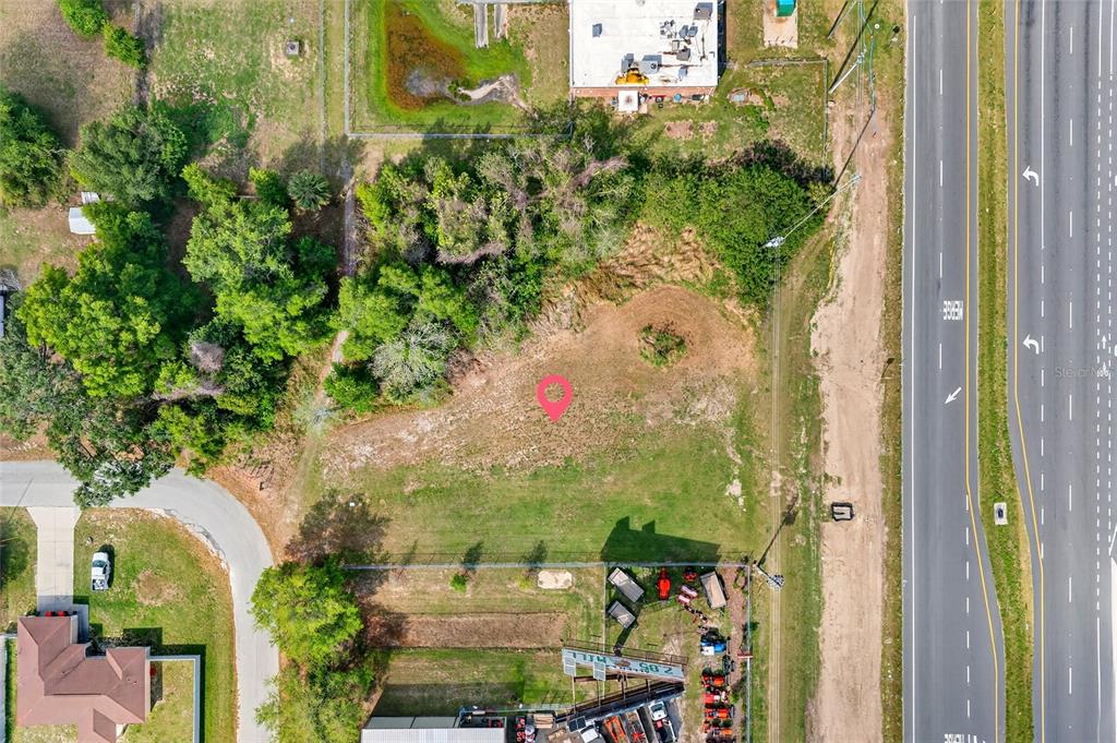 This aerial view shows a vacant, grassy lot situated between a road and a wooded area — HWY 326 / NW 70TH, OCALA, FL