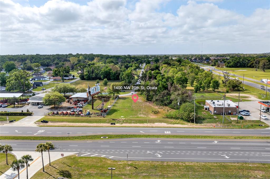 An aerial view shows a vacant, grassy lot situated between a commercial business and a road — HWY 326 / NW 70TH, OCALA, FL
