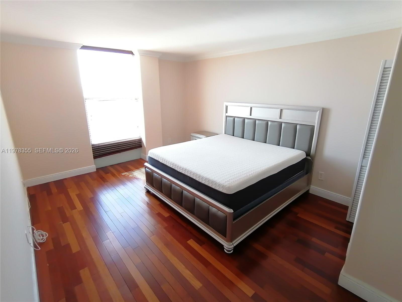 A bedroom features a bed with a gray headboard, hardwood floors, and a window — 2020 NE 135th St # 506, North Miami FL 33181, NORTH MIAMI, FL