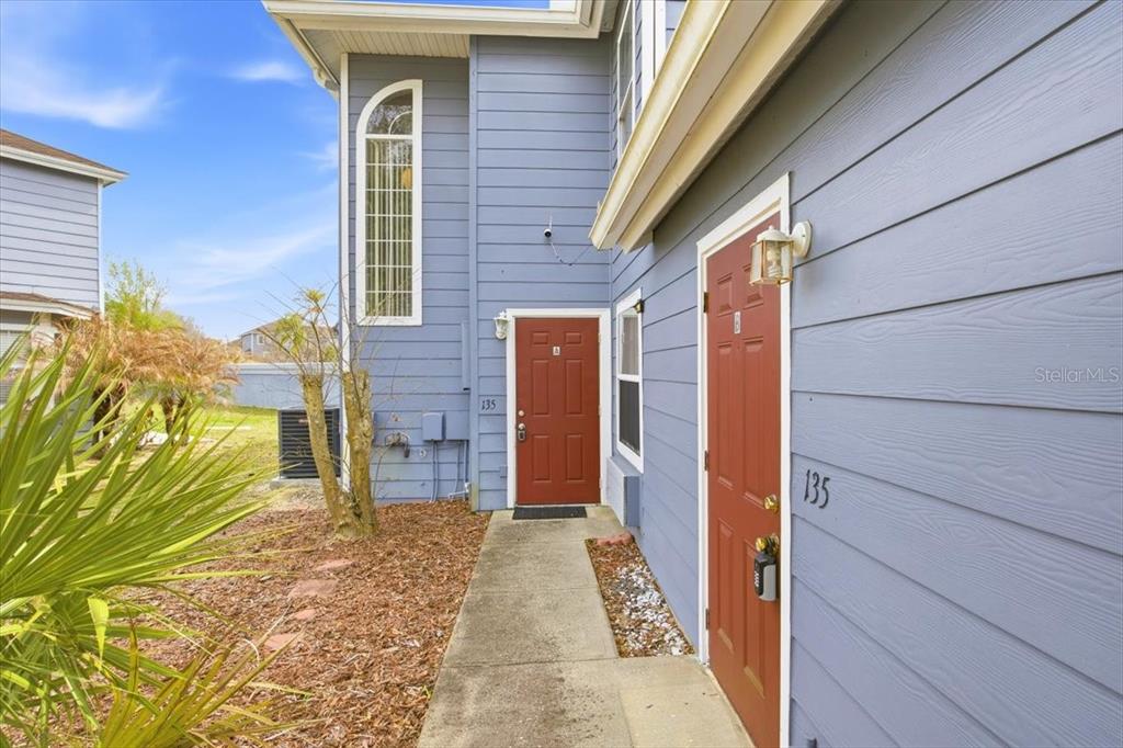A blue-sided building exterior features two red doors labeled 135 and a concrete walkway — 135 ORCHID DRIVE, DAVENPORT, FL
