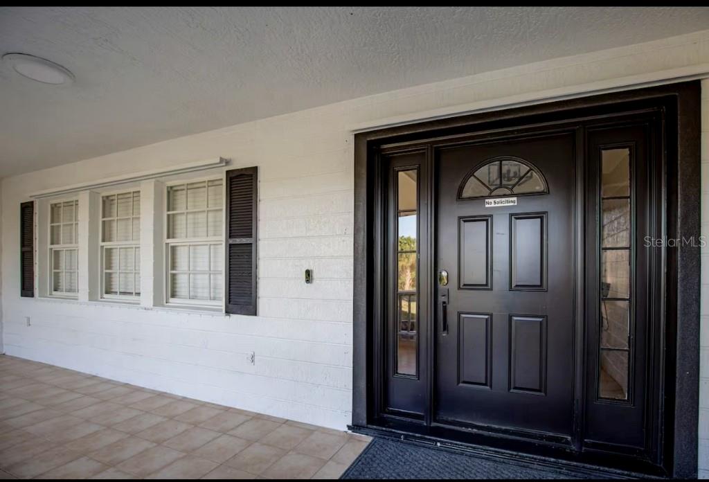 A front porch with a tiled floor, white siding, and a dark brown front door — 2089 SANDIA STREET, PORT CHARLOTTE, FL