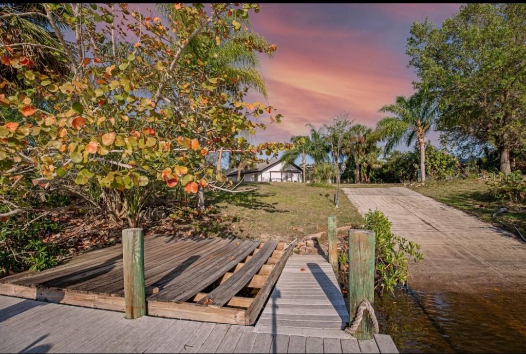 A wooden dock leads to a concrete boat ramp on a grassy waterfront property — 2089 SANDIA STREET, PORT CHARLOTTE, FL