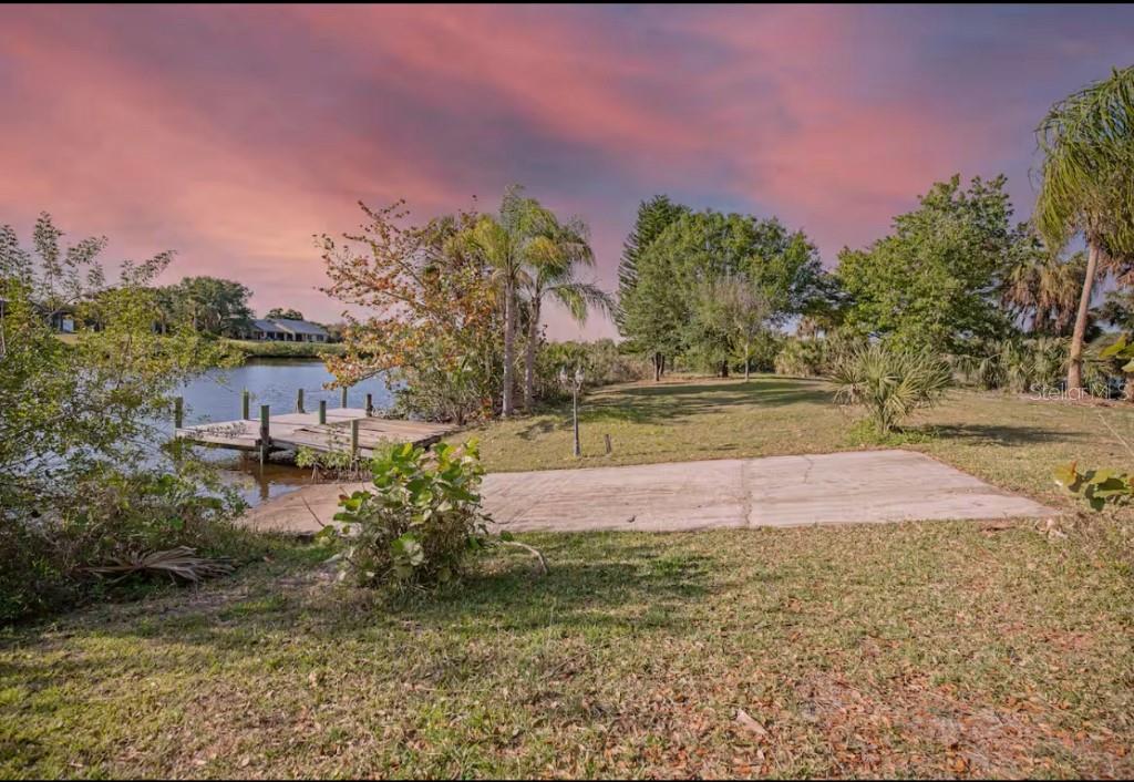 A concrete boat ramp leads into a lake next to a wooden dock and trees — 2089 SANDIA STREET, PORT CHARLOTTE, FL