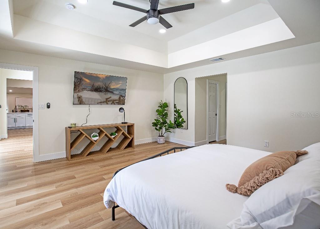 A bedroom features a tray ceiling, light wood flooring, a television, and a wooden console table — 2089 SANDIA STREET, PORT CHARLOTTE, FL