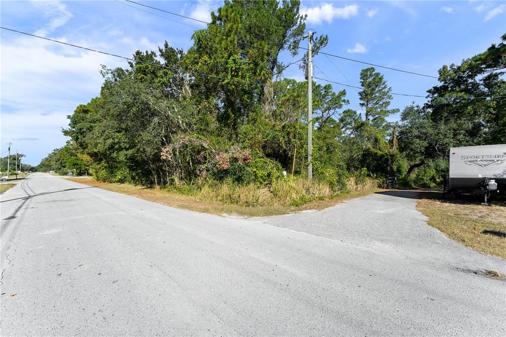 A paved road forks toward a wooded lot with a utility pole and a camper — 7049 CENTERWOOD AVENUE, SPRING HILL, FL