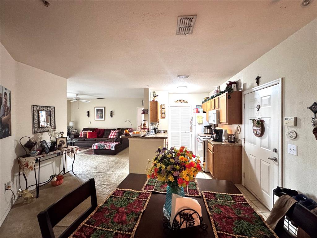 A dining area with a floral centerpiece leads into a kitchen and a carpeted living room — 5550 E MICHIGAN STREET UNIT 2112, ORLANDO, FL