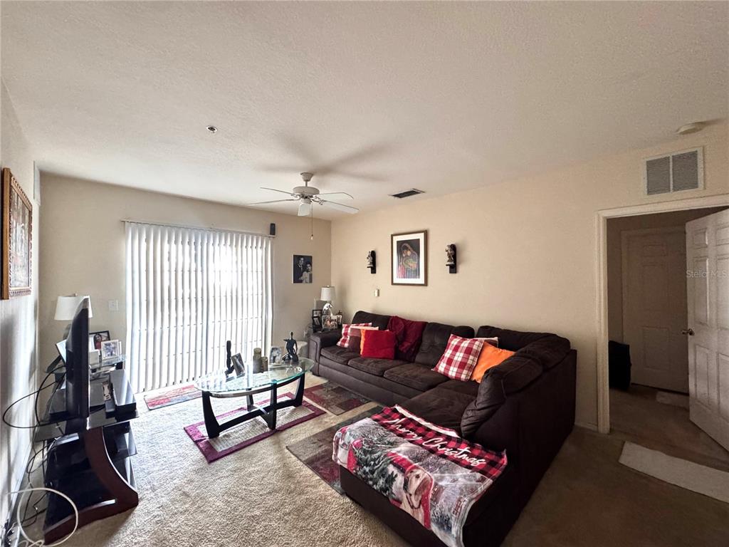 A living room features a large brown sectional sofa, a glass coffee table, and vertical blinds — 5550 E MICHIGAN STREET UNIT 2112, ORLANDO, FL