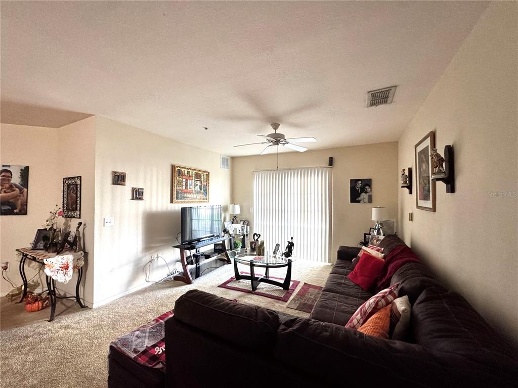 A living room features a dark sectional sofa, a television on a stand, and carpeted flooring — 5550 E MICHIGAN STREET UNIT 2112, ORLANDO, FL