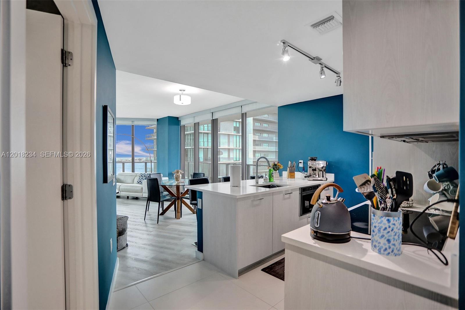 A modern kitchen with white cabinets and a blue accent wall overlooks a dining area — 501 NE 31st St # 3706, Miami FL 33137, MIAMI, FL