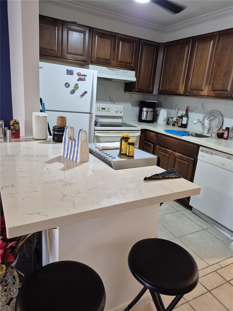 A kitchen features dark wood cabinets, white appliances, and a light-colored quartz breakfast bar — 371 brighton I # 371, Boca Raton FL 33434, BOCA RATON, FL