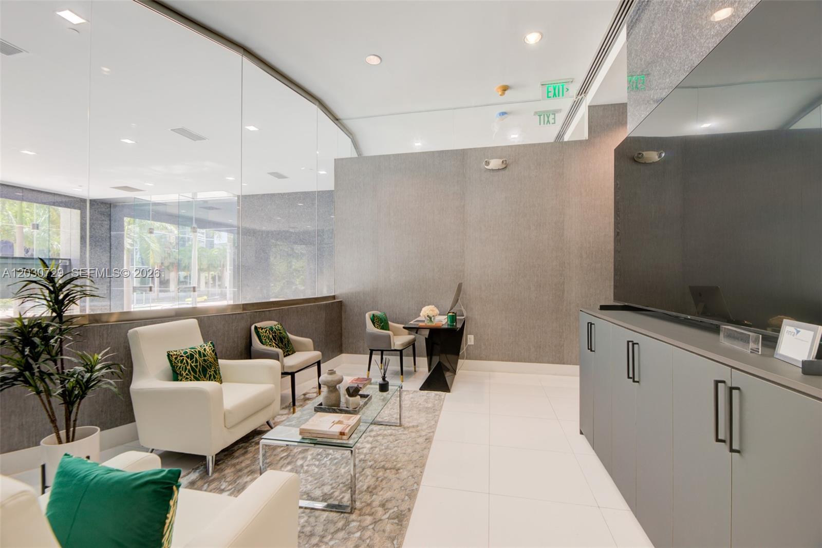 A modern office lobby features white armchairs, a glass coffee table, and a sleek desk — 1200 Brickell Ave # K, Miami FL 33131, MIAMI, FL