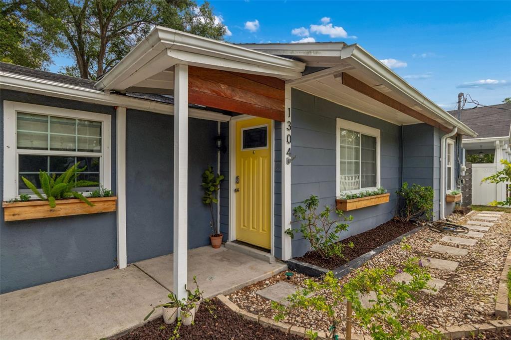 A gray house exterior features a bright yellow front door and wooden window boxes — 1304 E KNOLLWOOD STREET, TAMPA, FL