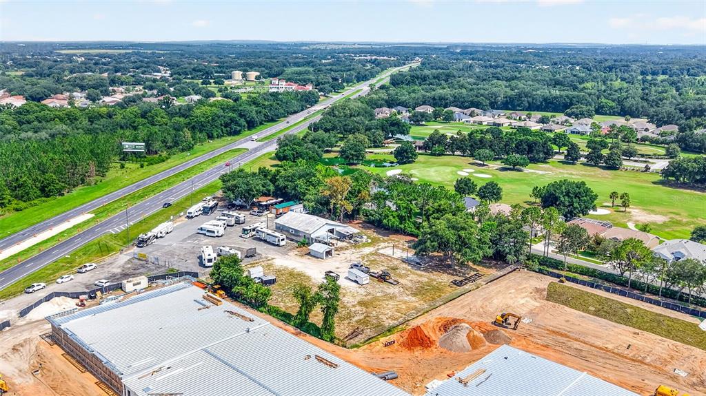 An aerial view shows a construction site with metal-roofed buildings, parked RVs, and nearby roads — 27101 US HIGHWAY 27, LEESBURG, FL