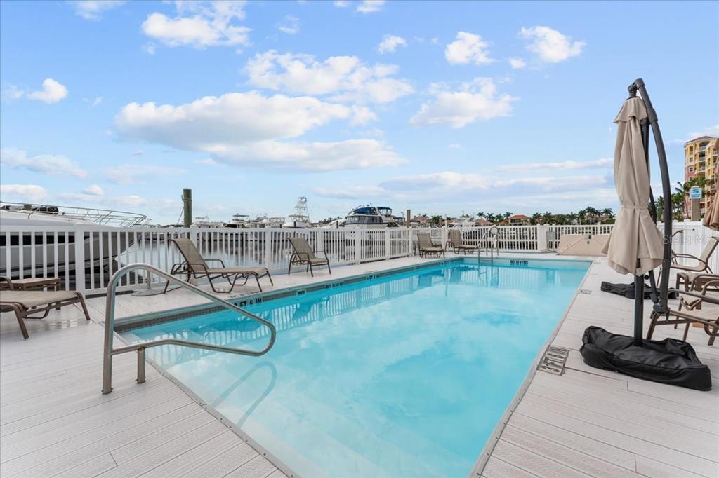 A rectangular swimming pool sits on a deck overlooking a marina with docked boats — 102 RIVIERA DUNES WAY UNIT C-7, PALMETTO, FL