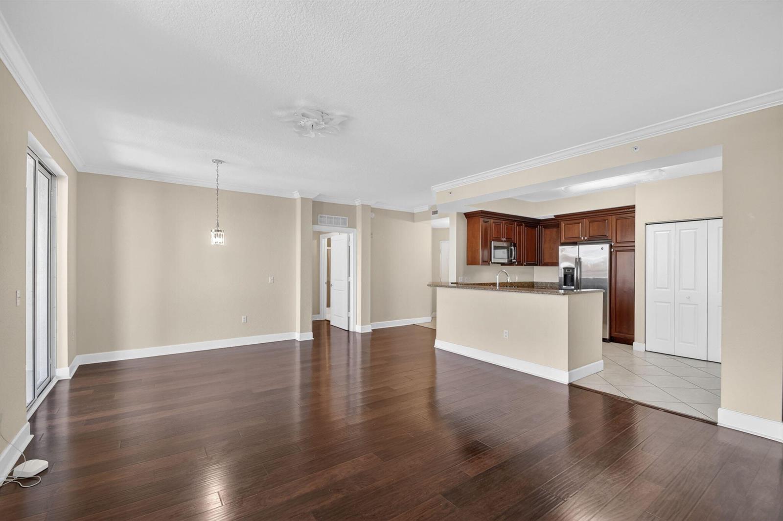 An open-concept living area with dark hardwood floors, a kitchen island, and beige walls — 1660 Renaissance Commons Boulevard # 2517, Boynton Beach FL 33426, BOYNTON BEACH, FL