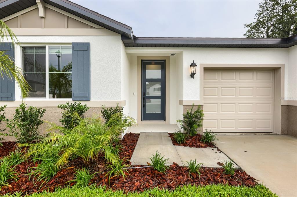A single-story house exterior features a dark gray front door, a beige garage, and landscaping — 3819 ORANGE FOREST LANE, BARTOW, FL
