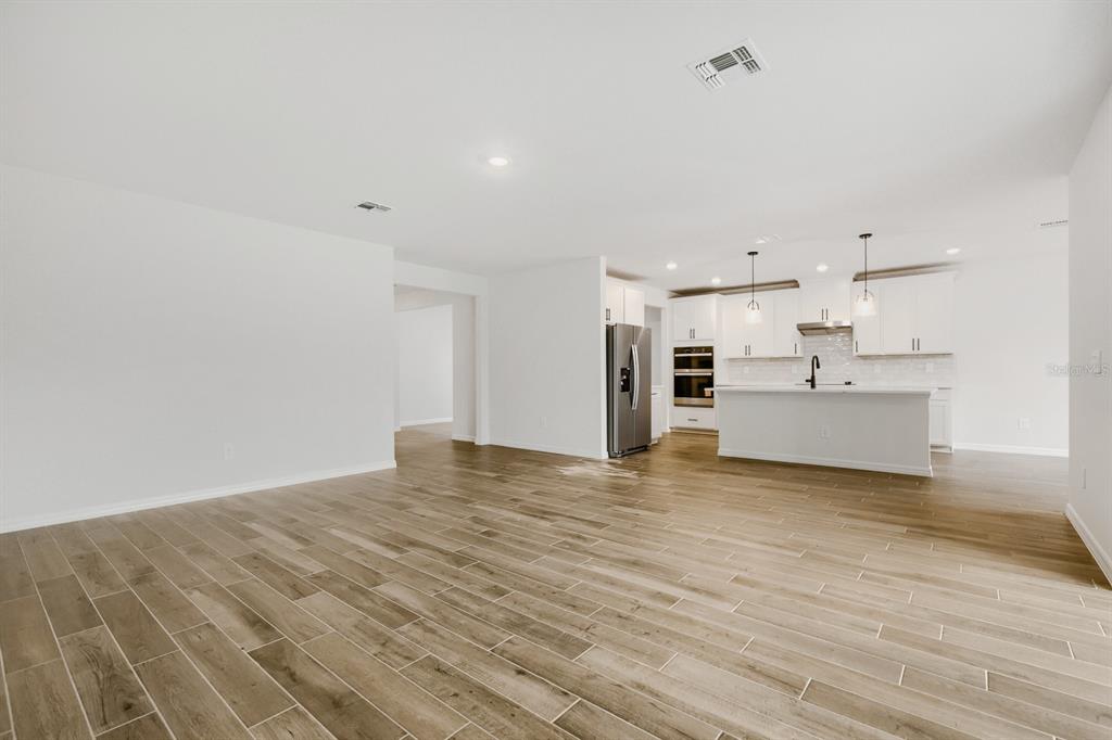An open-concept kitchen and living area featuring white cabinetry, stainless appliances, and wood-look tile flooring — 3819 ORANGE FOREST LANE, BARTOW, FL