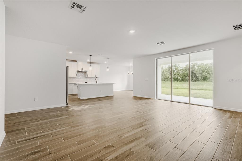 An open-concept living area features wood-look tile flooring, a white kitchen, and sliding glass doors — 3819 ORANGE FOREST LANE, BARTOW, FL
