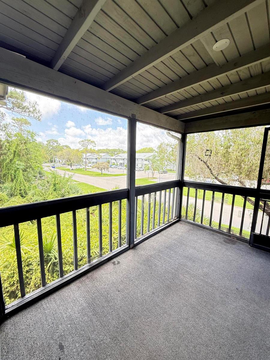 A screened-in balcony features a concrete floor, dark wooden railings, and views of trees and buildings — 8228 SE Croft Circle # 8, Hobe Sound FL 33455, HOBE SOUND, FL