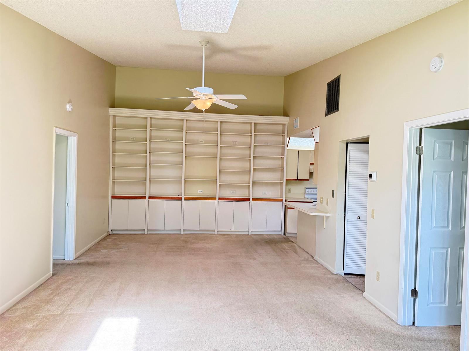 A living room features beige carpet, vaulted ceilings, a ceiling fan, and built-in wall shelving — 8228 SE Croft Circle # 8, Hobe Sound FL 33455, HOBE SOUND, FL
