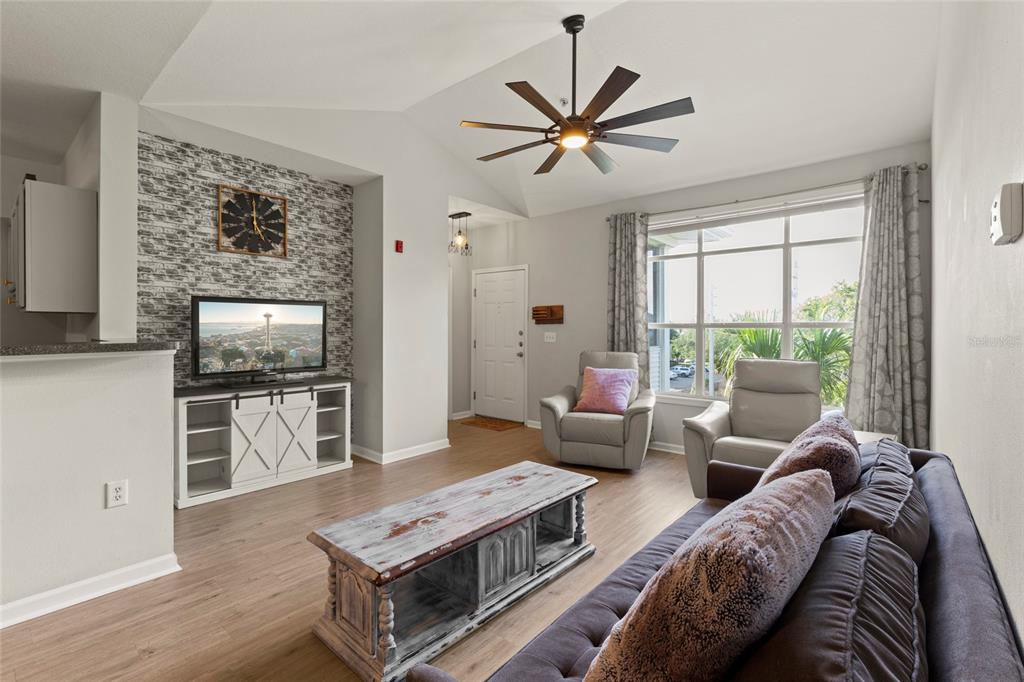A living room features a stone accent wall, wood-look flooring, and a ceiling fan — 4802 51ST STREET W UNIT 423, BRADENTON, FL
