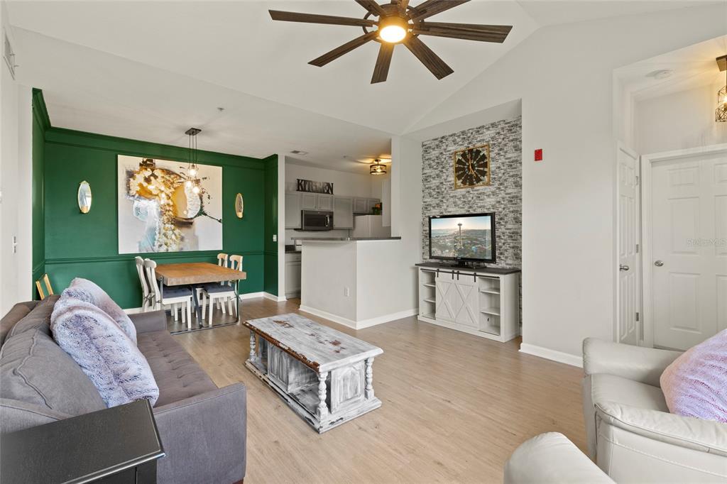 A living room and dining area with green accent walls, wood flooring, and a television — 4802 51ST STREET W UNIT 423, BRADENTON, FL
