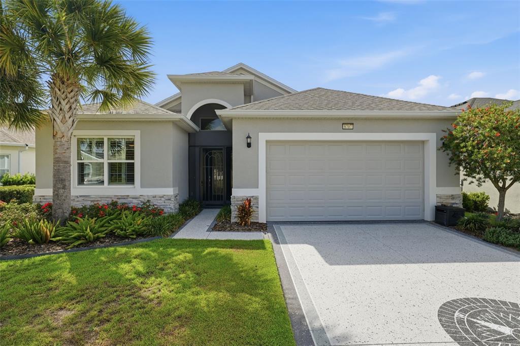 A single-story house with a gray garage, a compass design on the driveway, and palm trees — 8707 PROVIDENCE CT, MOUNT DORA, FL