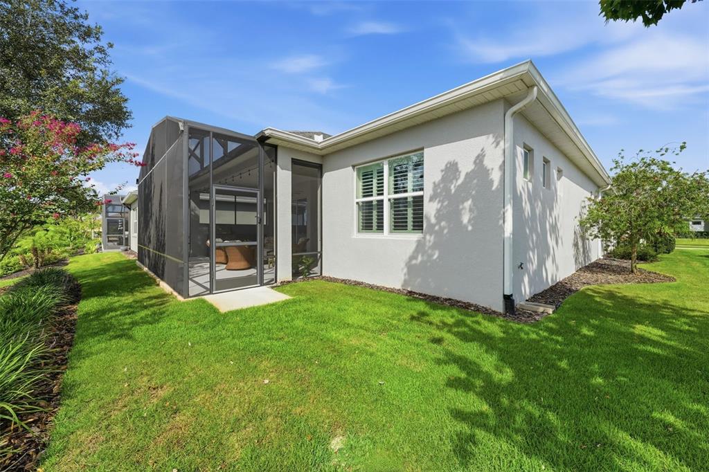 A view of a house exterior featuring a screened-in patio and a grassy backyard — 8707 PROVIDENCE CT, MOUNT DORA, FL