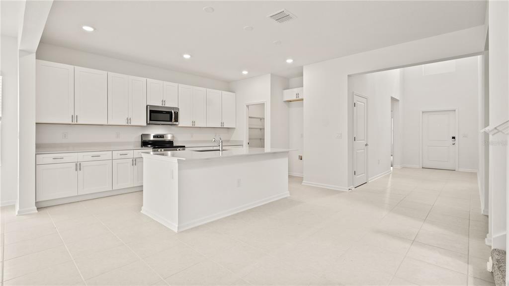 A modern kitchen features white cabinetry, stainless steel appliances, and a central island with countertops — 3323 ADDISON BOULEVARD, ST CLOUD, FL