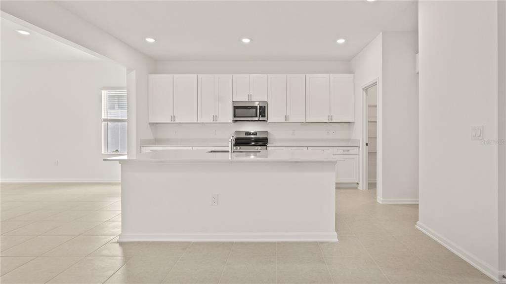 A modern kitchen features white cabinetry, stainless steel appliances, and a large central island — 3323 ADDISON BOULEVARD, ST CLOUD, FL