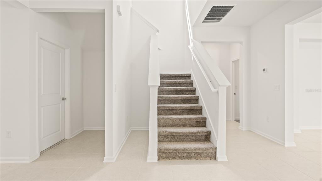 A carpeted staircase with white railings sits in a bright, white-walled entryway with tile flooring — 3323 ADDISON BOULEVARD, ST CLOUD, FL
