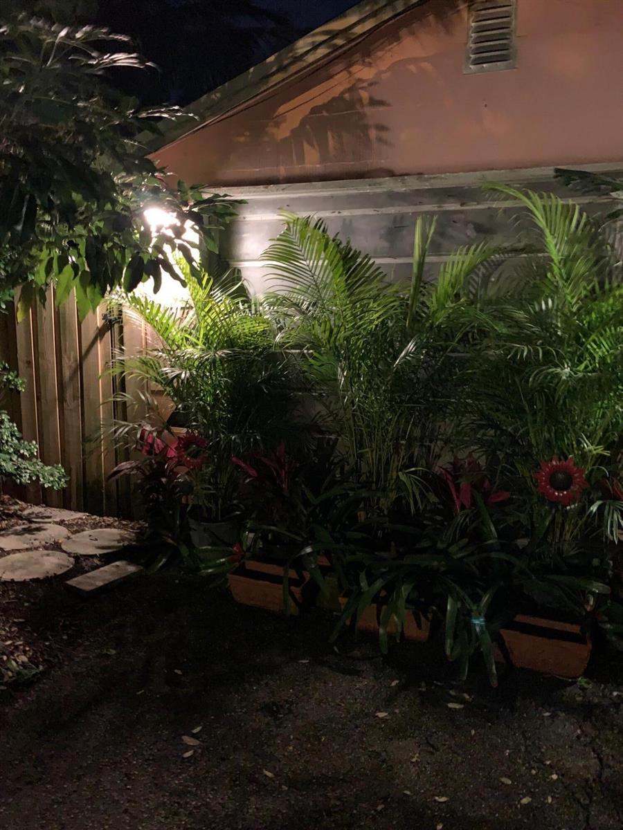 A nighttime view of a backyard garden featuring potted palm trees and decorative flowers — LAKE WORTH, FL