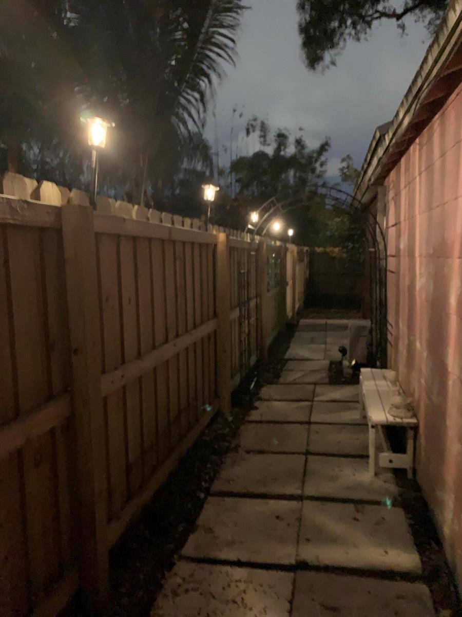 A narrow outdoor walkway features a wooden fence, stone pavers, and several small landscape lights — LAKE WORTH, FL