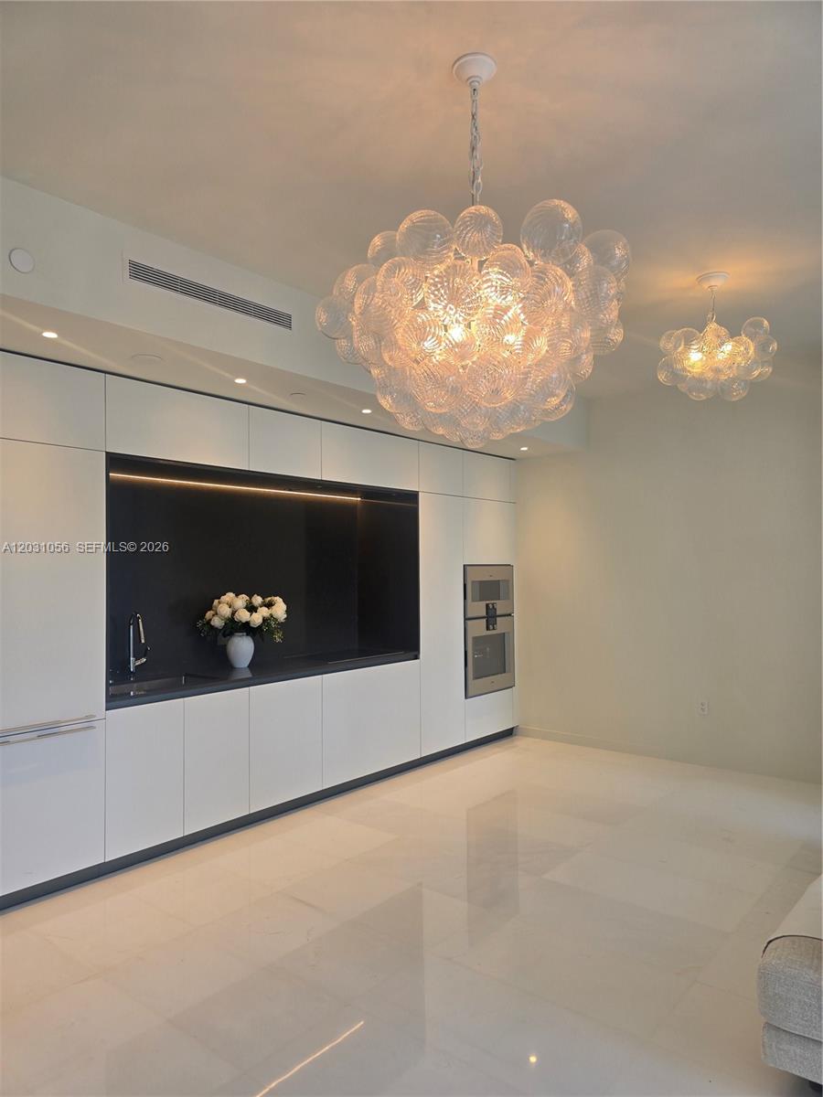 A modern kitchen features white cabinetry, a black recessed backsplash, and two glass bubble chandeliers — 300 Biscayne Blvd Way # 2408W, Miami FL 33131, MIAMI, FL