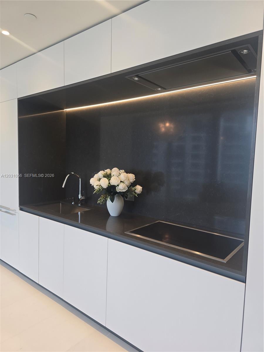 A modern kitchen features white cabinetry, a dark stone countertop, and a built-in cooktop — 300 Biscayne Blvd Way # 2408W, Miami FL 33131, MIAMI, FL