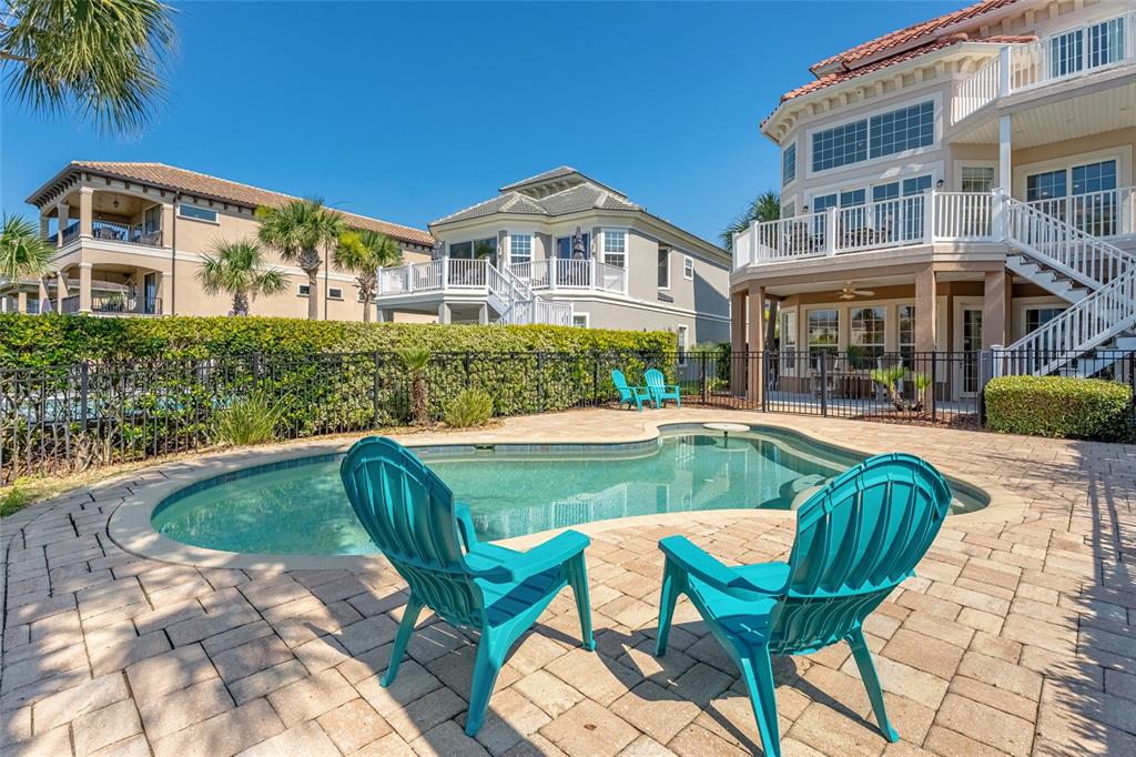 A swimming pool with turquoise chairs sits on a paved patio behind a large house — 29 NORTHSHORE AVENUE, PALM COAST, FL