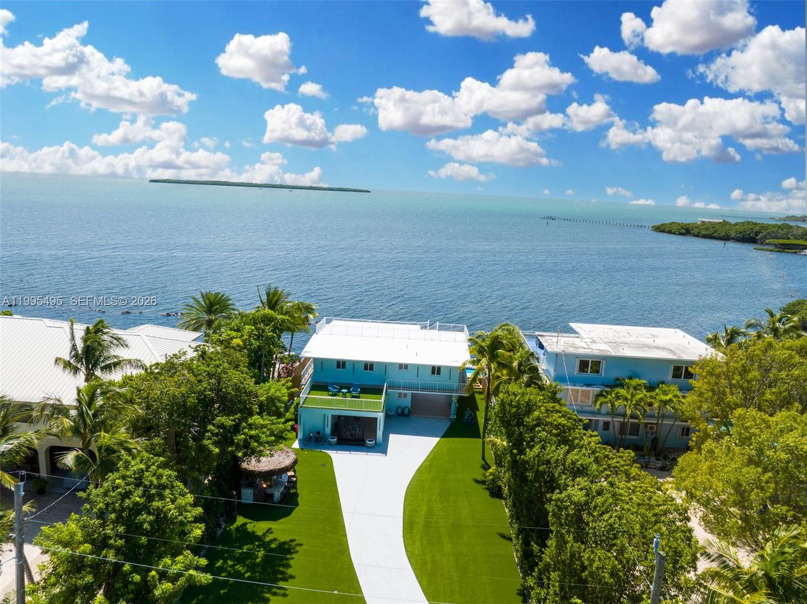 An aerial view shows a light blue house with a white roof near the ocean — 188 Orange Blossom Rd, Tavernier FL 33070, TAVERNIER, FL