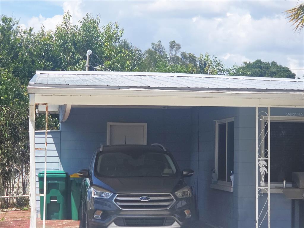 A dark gray Ford SUV is parked under a metal-roofed carport attached to a blue house — 11192 3RD AVENUE, PUNTA GORDA, FL