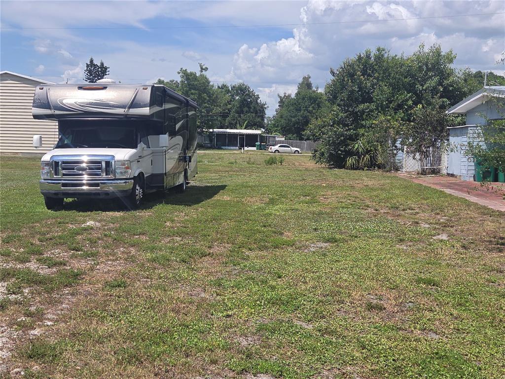 A large recreational vehicle is parked on a grassy lot next to a small house — 11192 3RD AVENUE, PUNTA GORDA, FL