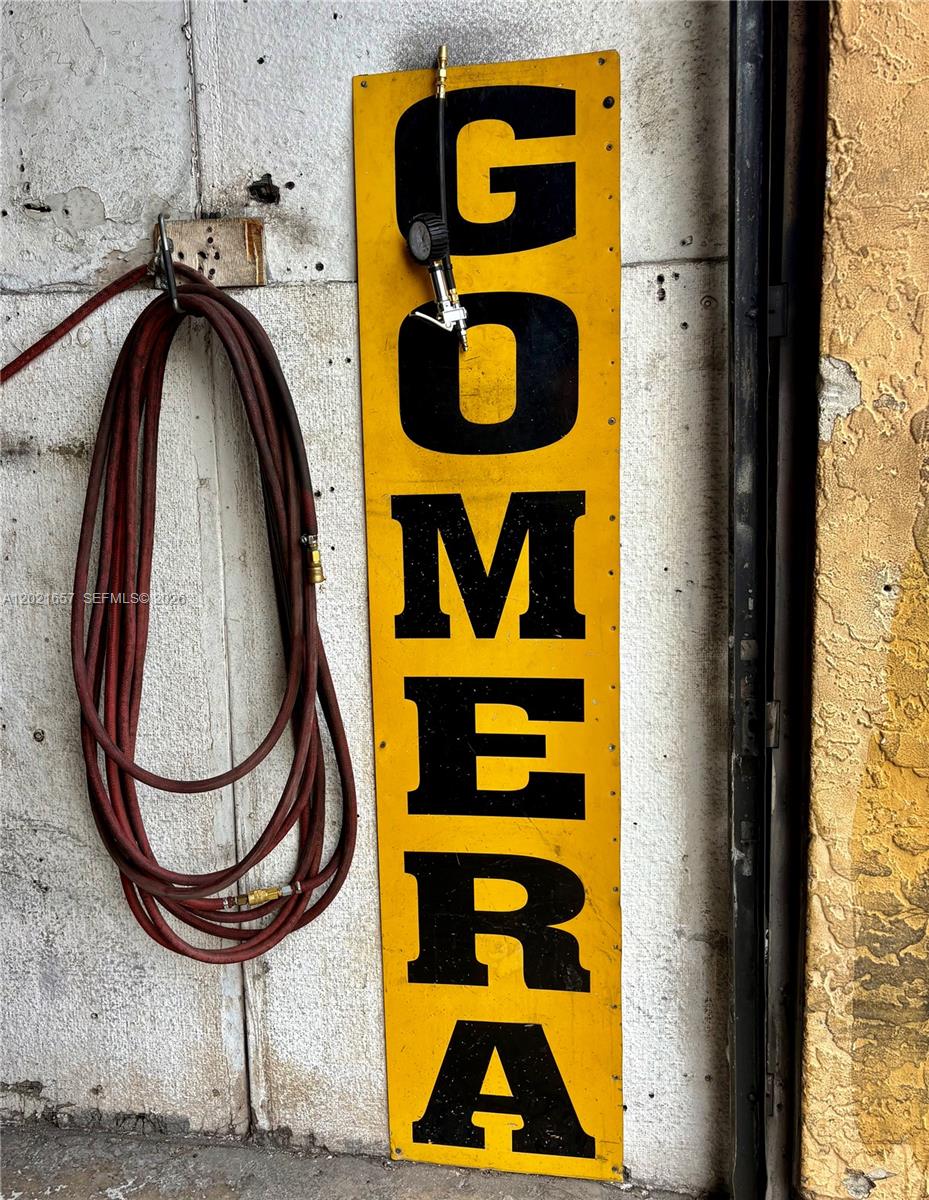 A yellow vertical sign reading GOMERA hangs on a textured wall next to a coiled hose — 11750 NW 87th Pl, Hialeah Gardens FL 33018, HIALEAH GARDENS, FL