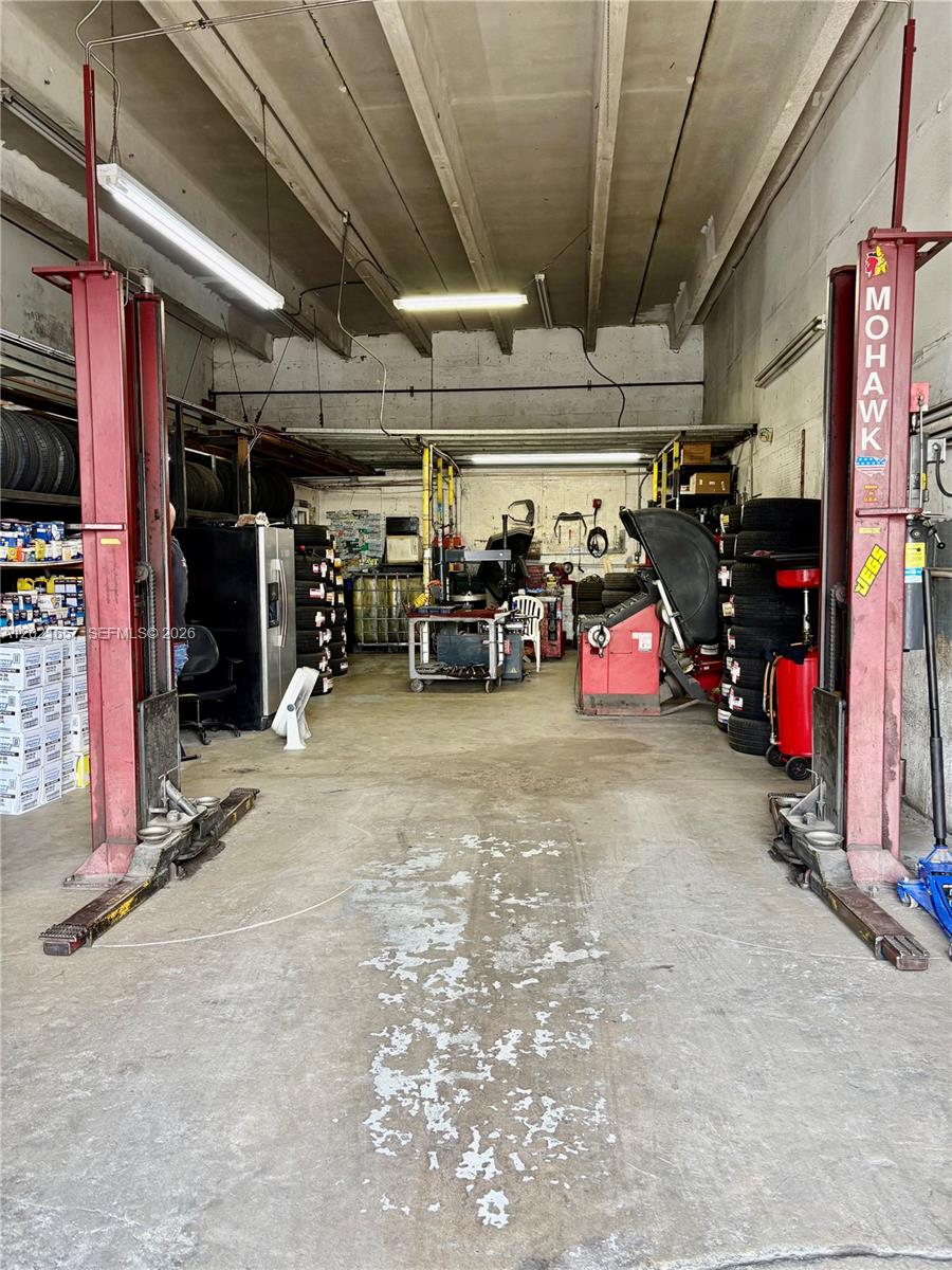 An auto repair shop interior features a two-post vehicle lift and tire service equipment — 11750 NW 87th Pl, Hialeah Gardens FL 33018, HIALEAH GARDENS, FL