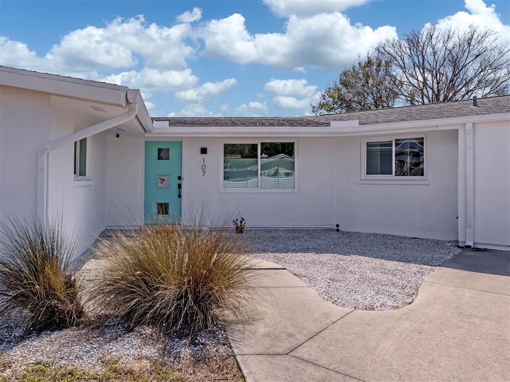 A white house exterior features a light blue front door and a gravel front yard — 107 SORRENTO DRIVE, OSPREY, FL