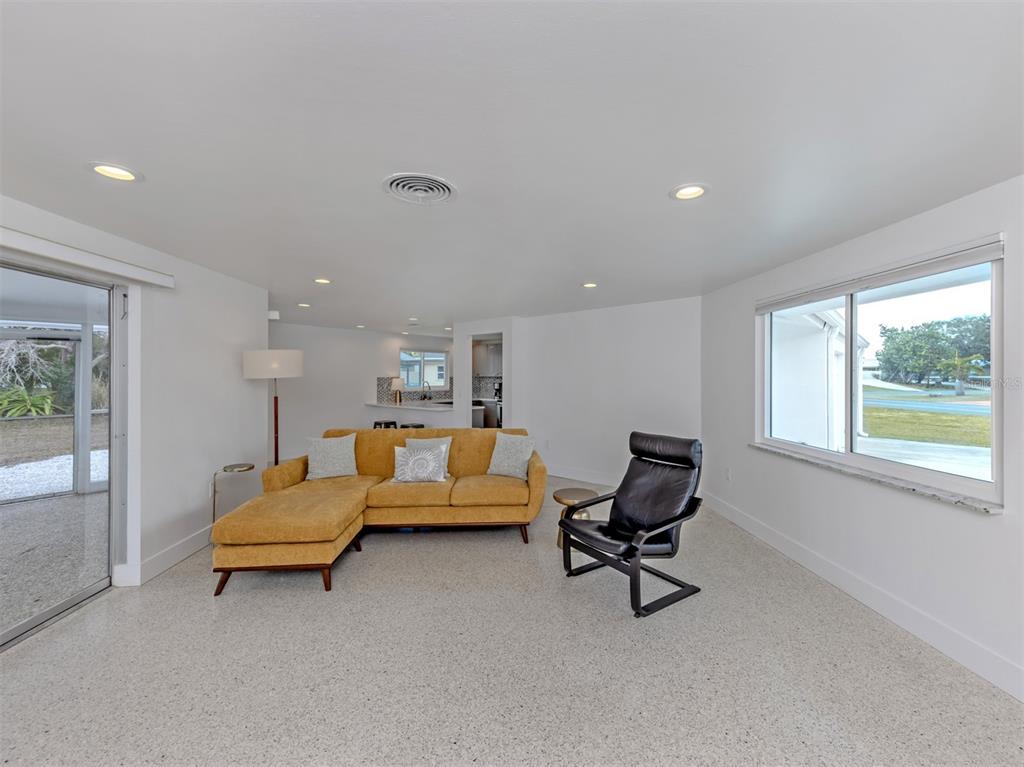 A living room features a yellow sectional sofa, a black chair, and white walls — 107 SORRENTO DRIVE, OSPREY, FL