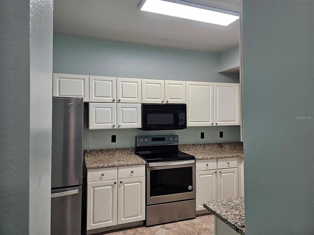 A kitchen features white cabinets, granite countertops, and stainless steel appliances — 5506 METROWEST BOULEVARD UNIT 13-103, ORLANDO, FL