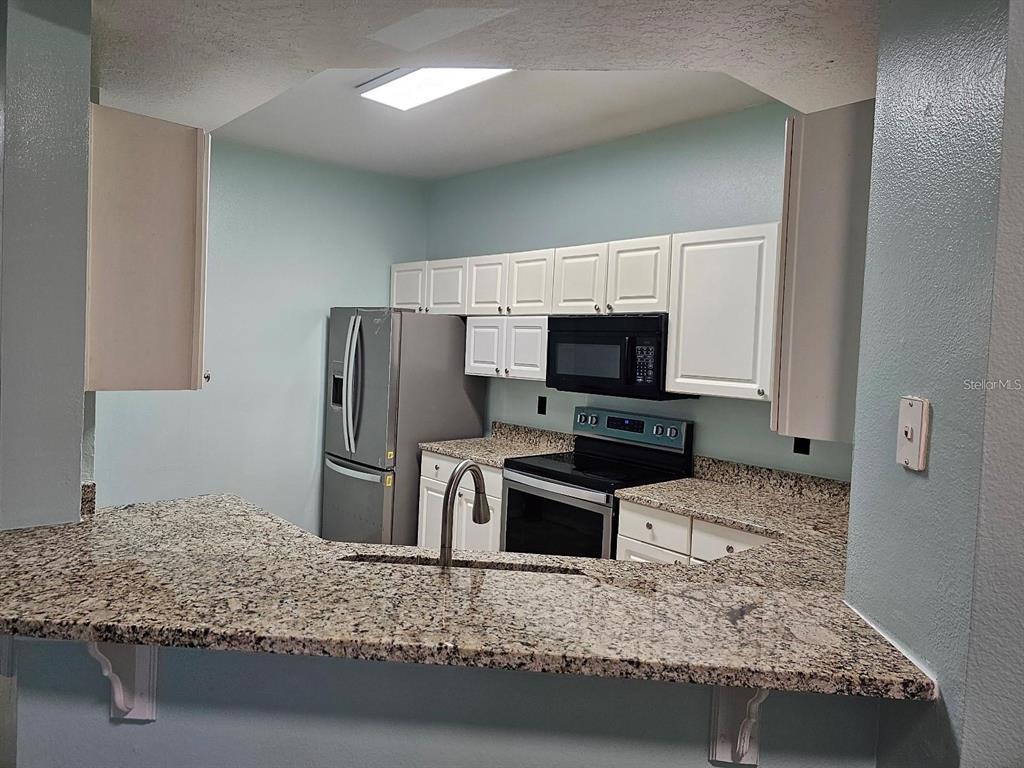 A kitchen features white cabinets, granite countertops, stainless steel appliances, and a breakfast bar — 5506 METROWEST BOULEVARD UNIT 13-103, ORLANDO, FL