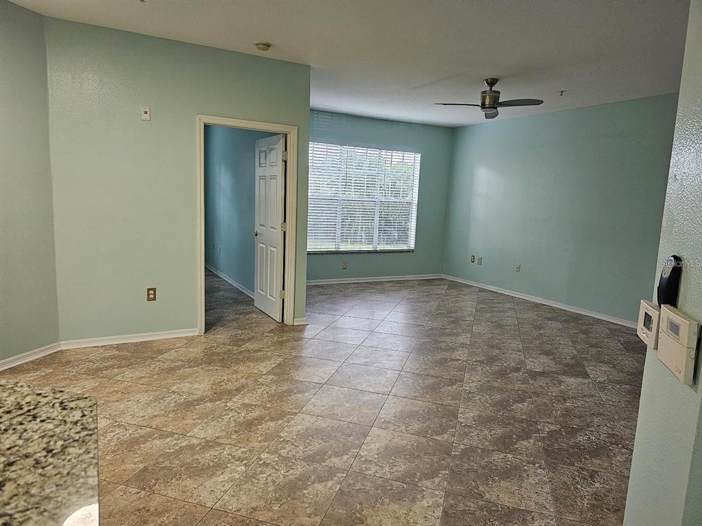 An open living area features light blue walls, tiled floors, and a ceiling fan — 5506 METROWEST BOULEVARD UNIT 13-103, ORLANDO, FL