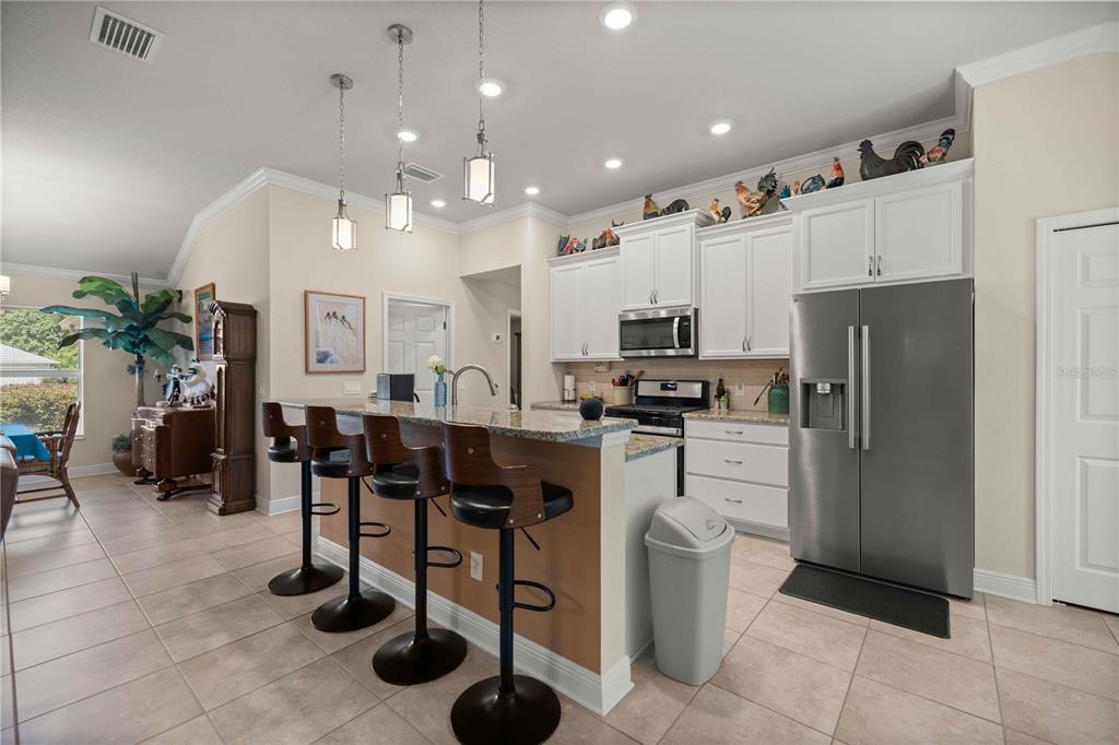 A kitchen with white cabinets, stainless steel appliances, a granite island, and four bar stools — 3125 N CANTERBURY LAKE DRIVE, HERNANDO, FL