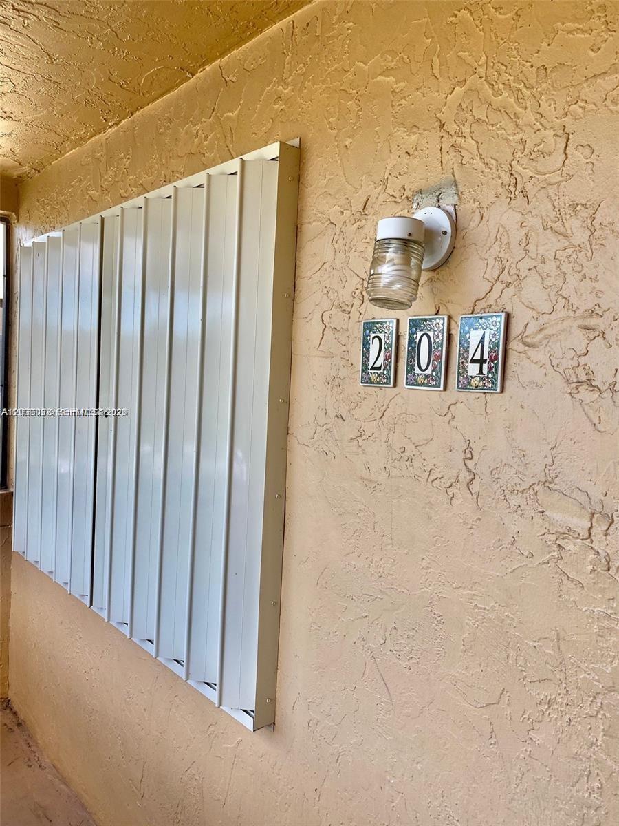 A beige exterior wall features a white accordion hurricane shutter and the house number 204 — WESTON, FL