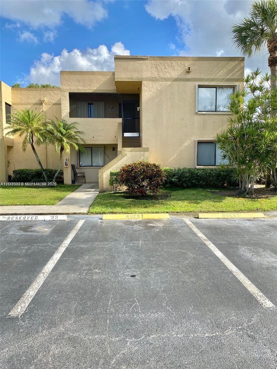 A two-story tan stucco apartment building features a ground-level entrance and designated parking spaces — WESTON, FL